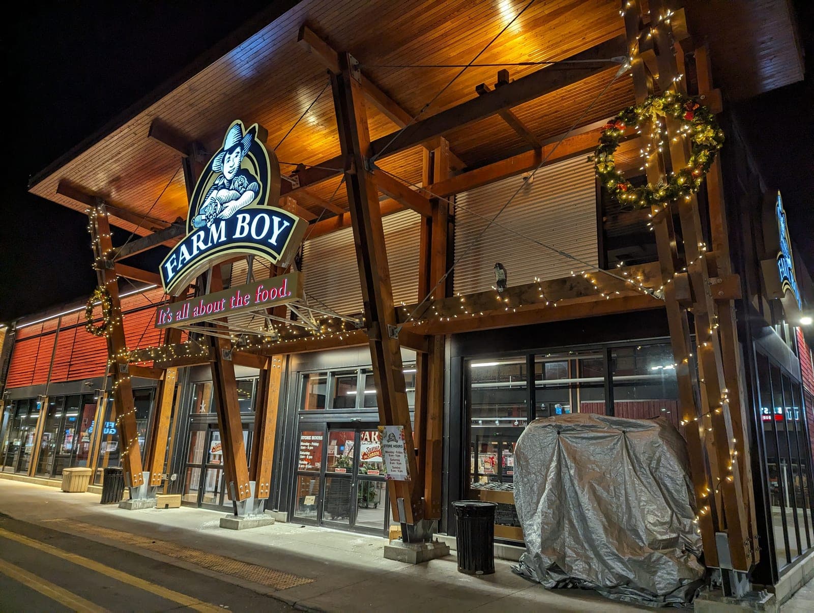 Commercial storefront facade lined with warm-white Christmas lights and a lit wreath at night