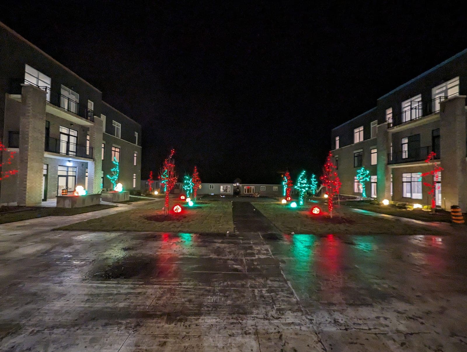 Symmetrical commercial courtyard lit with red and green Christmas trees and warm-white building lights