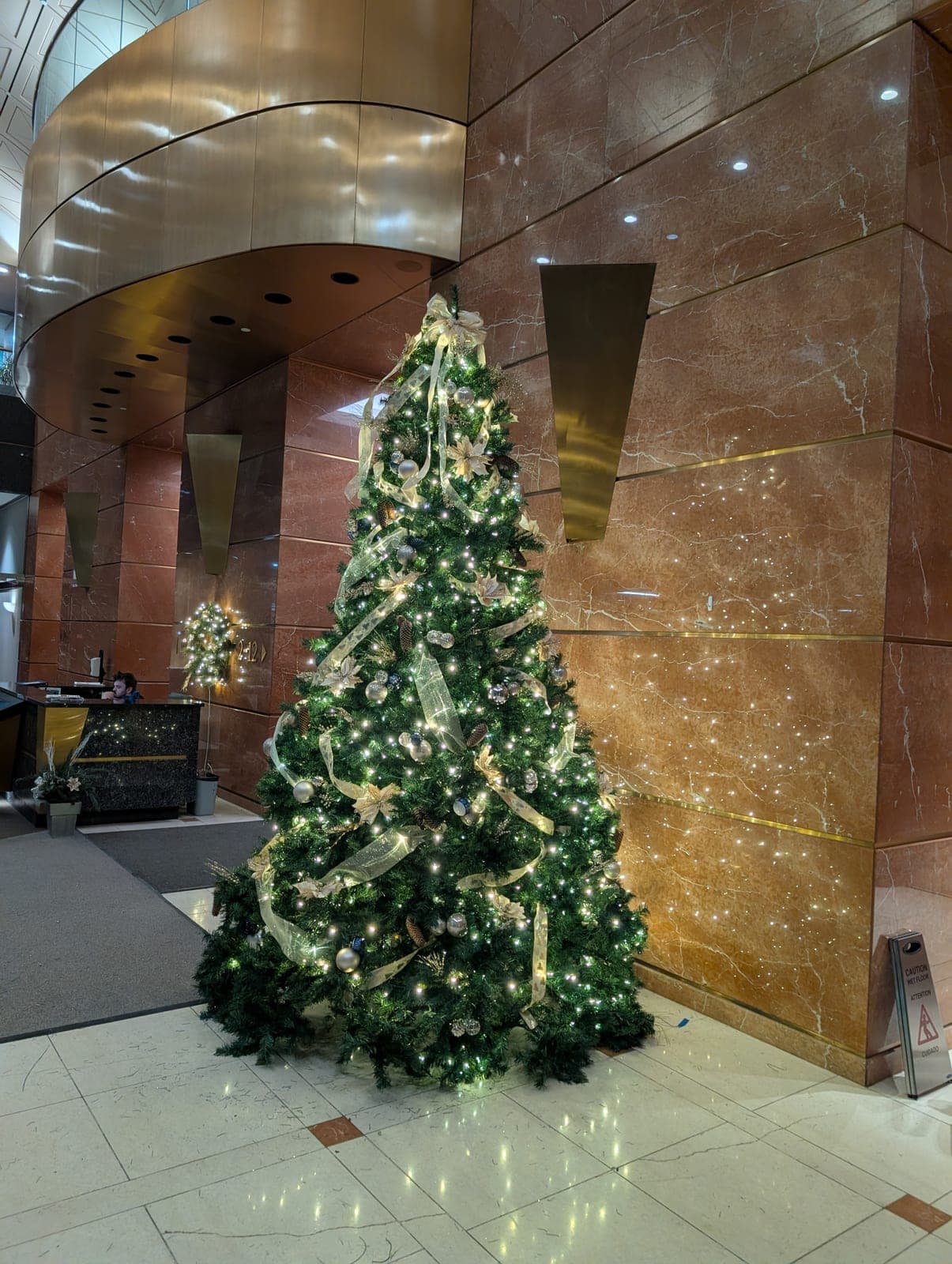 Large professionally decorated Christmas tree with gold ribbon in a corporate marble lobby.