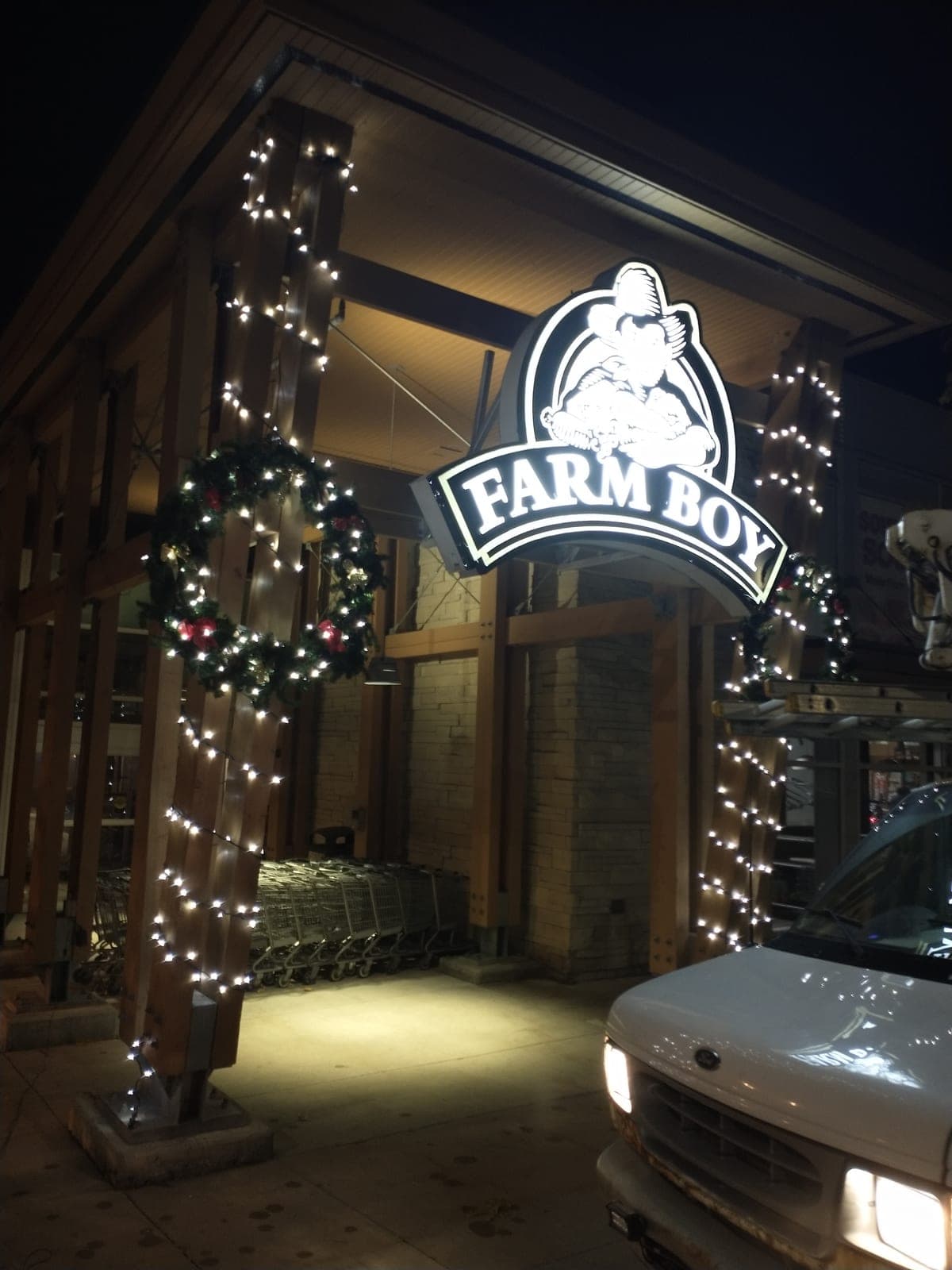 Grocery storefront entrance with garland-wrapped posts, warm-white Christmas lights and a lit wreath