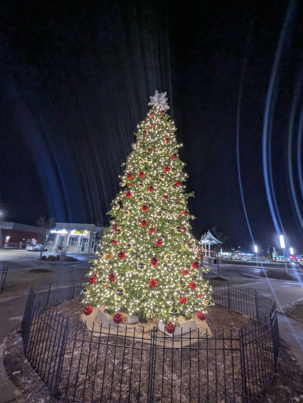 Illuminated commercial Christmas tree with red ornaments in a shopping-centre courtyard at night