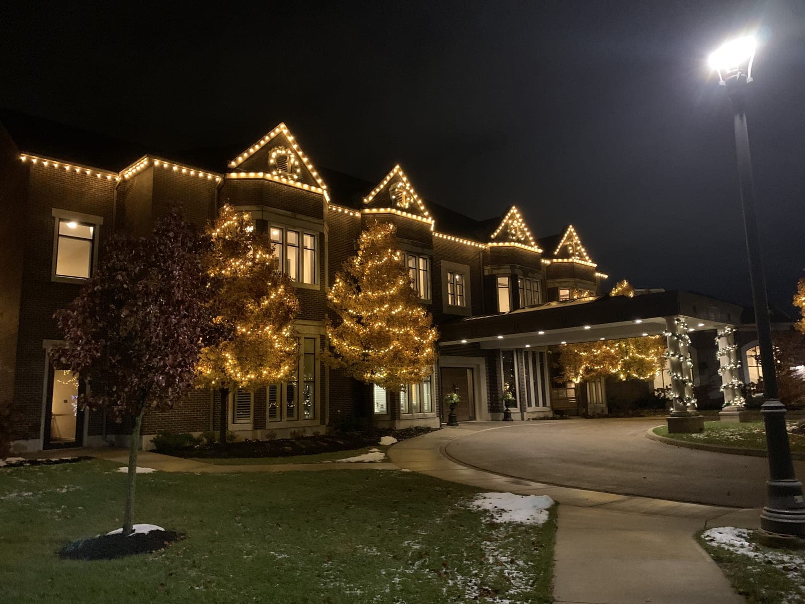 Luxury venue with warm-white roofline Christmas lights and mature trees wrapped in lights along the driveway