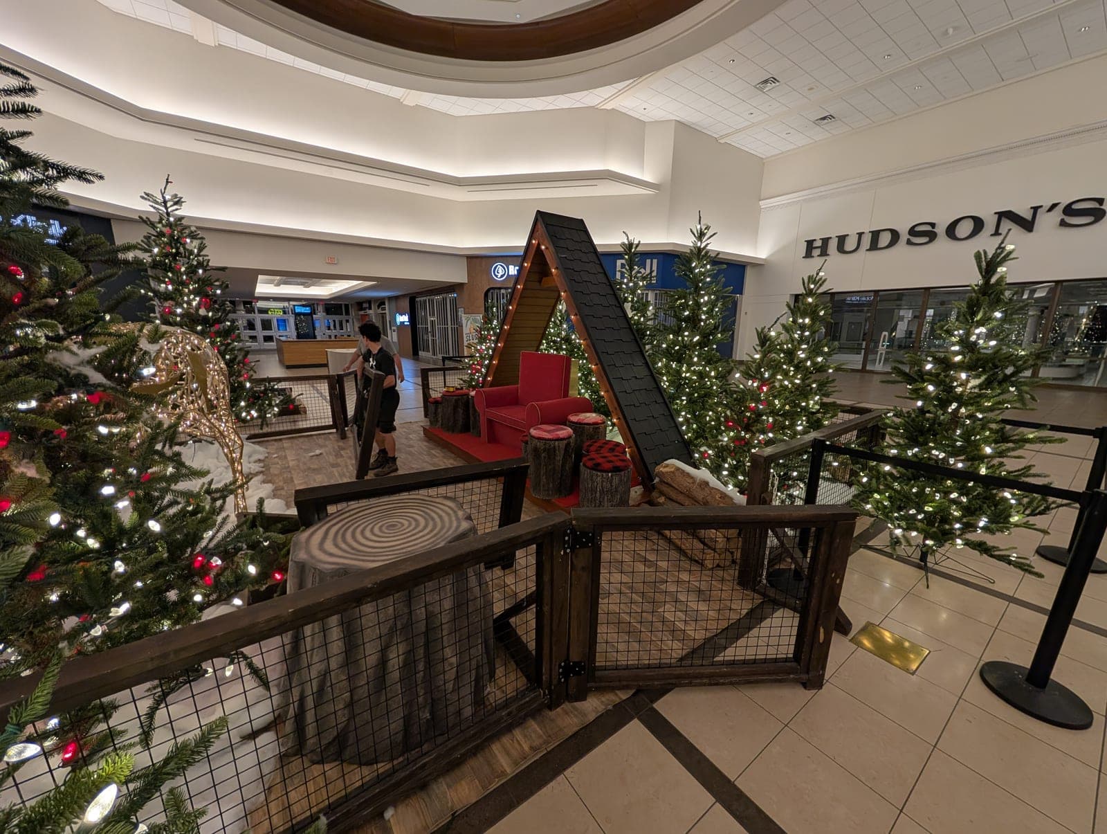 Rustic A-frame photo setup surrounded by lit Christmas trees in a shopping mall.