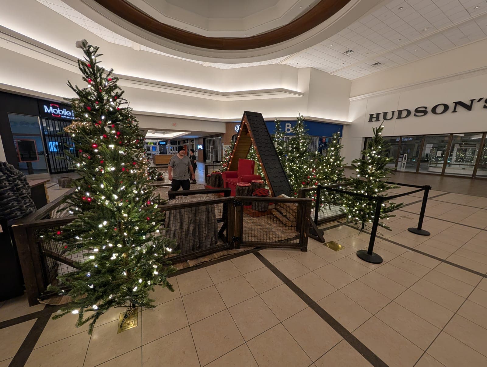 Decorated Christmas trees and a rustic photo set lining a shopping mall concourse.