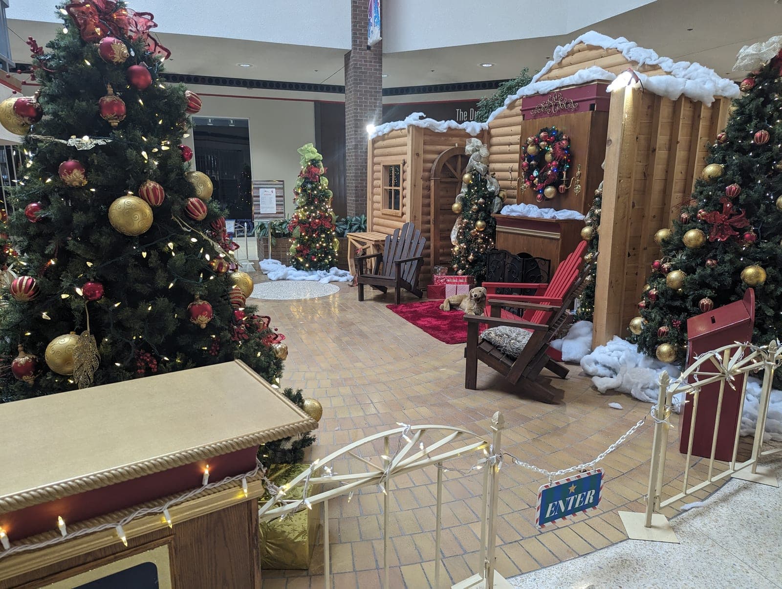 Shopping mall Santa's cabin holiday display framed by richly decorated Christmas trees