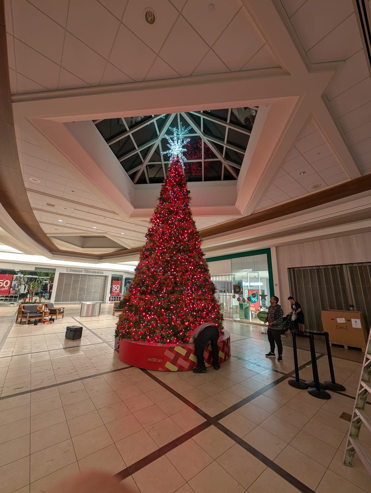 Towering red and green Christmas tree display in a shopping mall atrium.