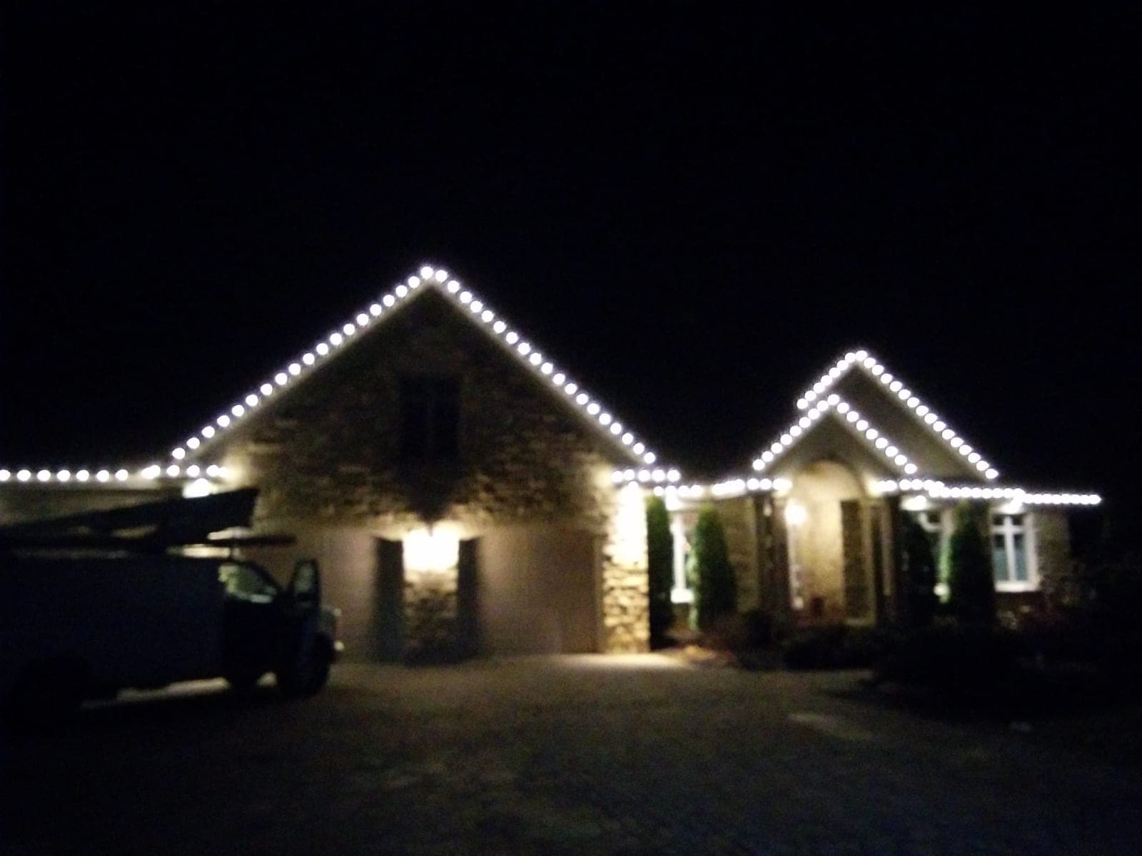 Stone home with warm-white Christmas lights crisply outlining two gable rooflines at night