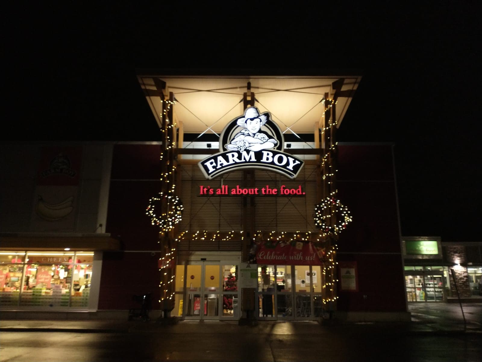 Commercial storefront facade with warm-white Christmas lights, garland-wrapped columns and lit wreaths